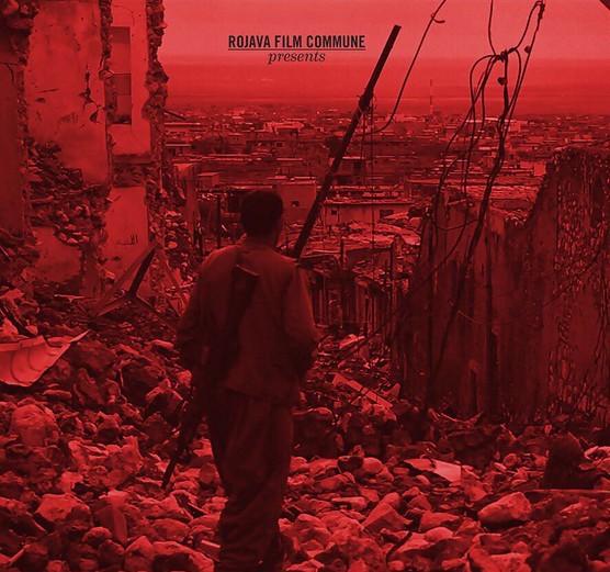 Seen from behind a man is looking through the walls of a destroyed house at a city. The image is tinted red.